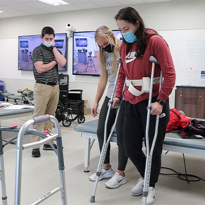 a masked patient takes steps during a physical therapy session 