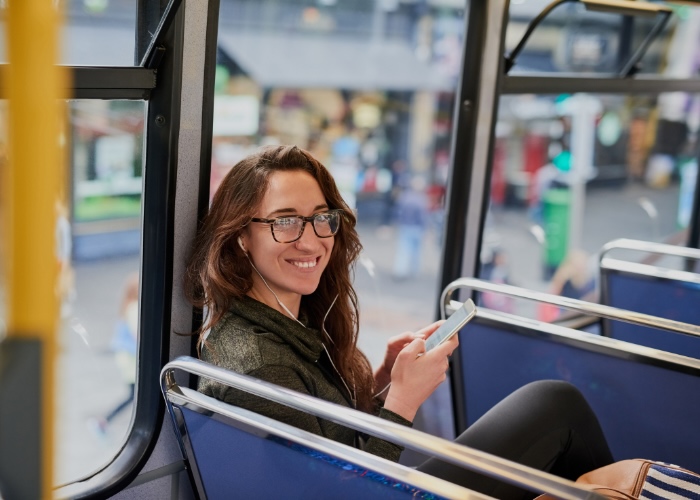 Woman on bus wearing headphones connected to her cell phone.