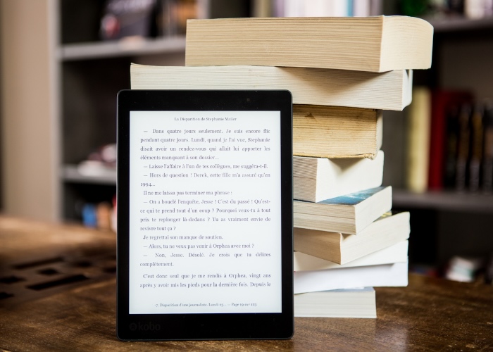 Tablet with a book on the screen leaning against a pile of paper books.