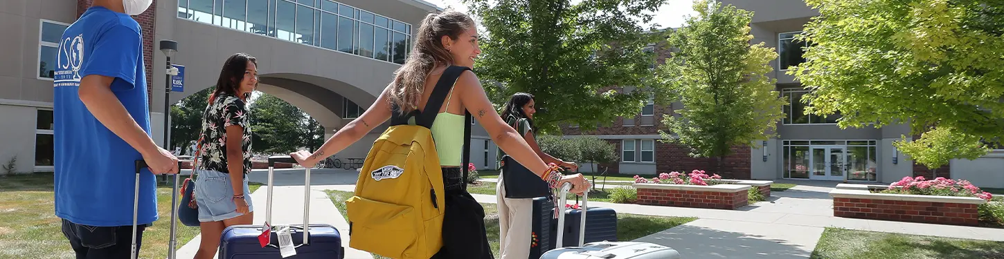 students carrying suitcases across campus