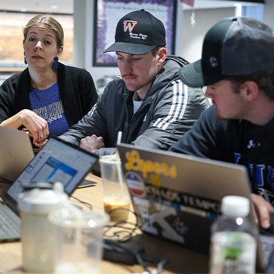 students and an instructor sit at a table with laptops