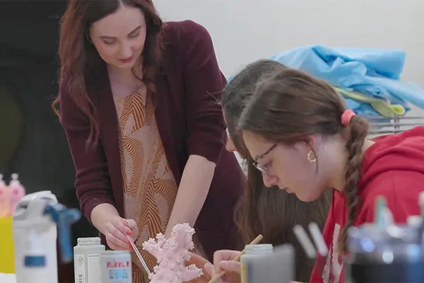 a teacher works with a student in an art class