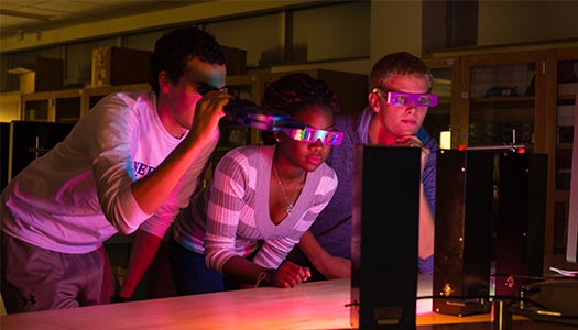 three students view a laser in a dark classroom