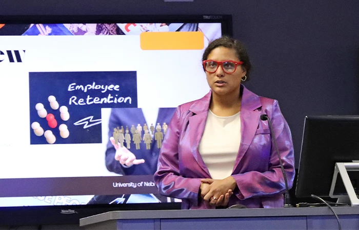 a student stands behind a desk, giving a presentation