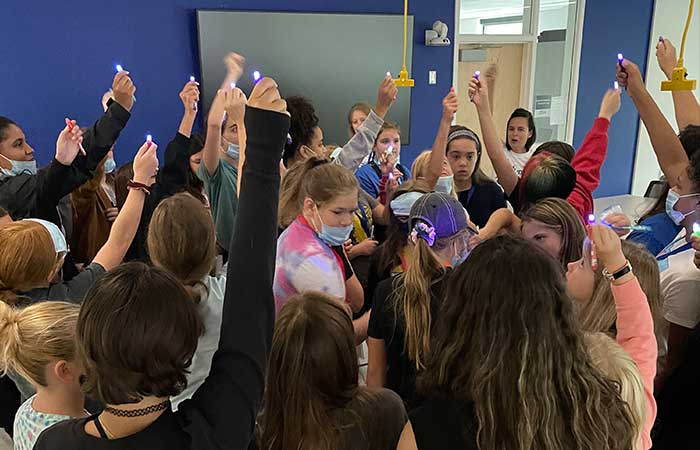 students participate in an activity, holding lights above their heads