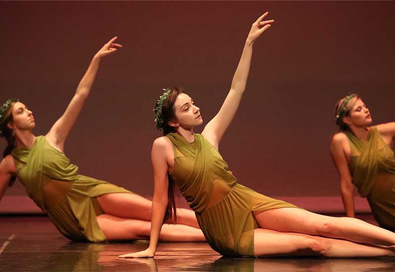 three students in green dresses perform a dance piece