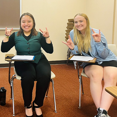 students pose for a photo sitting at desks throwing the lopes