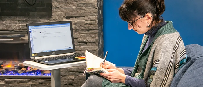 a student journals in front of her laptop in a student common area