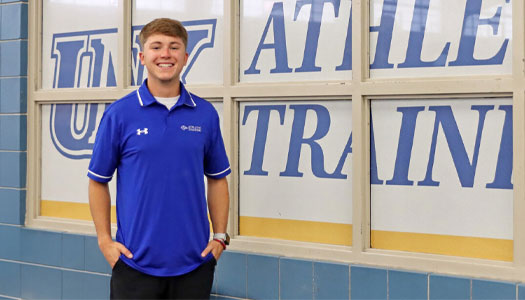 Ethan Twohig poses for a photo in front of a window with athletic training decals