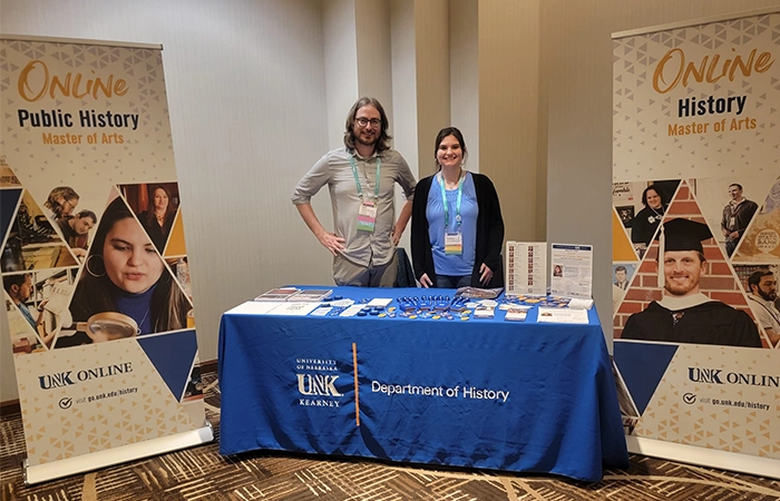 a student and professor man a booth at a conference