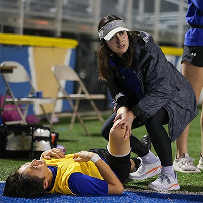 a student works with an athlete on the sidelines
