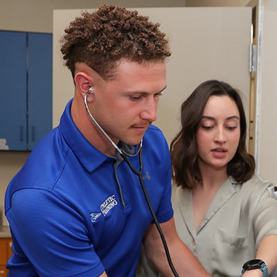 a student and instructor work with a dummy (offscreen) in a clinical setting 