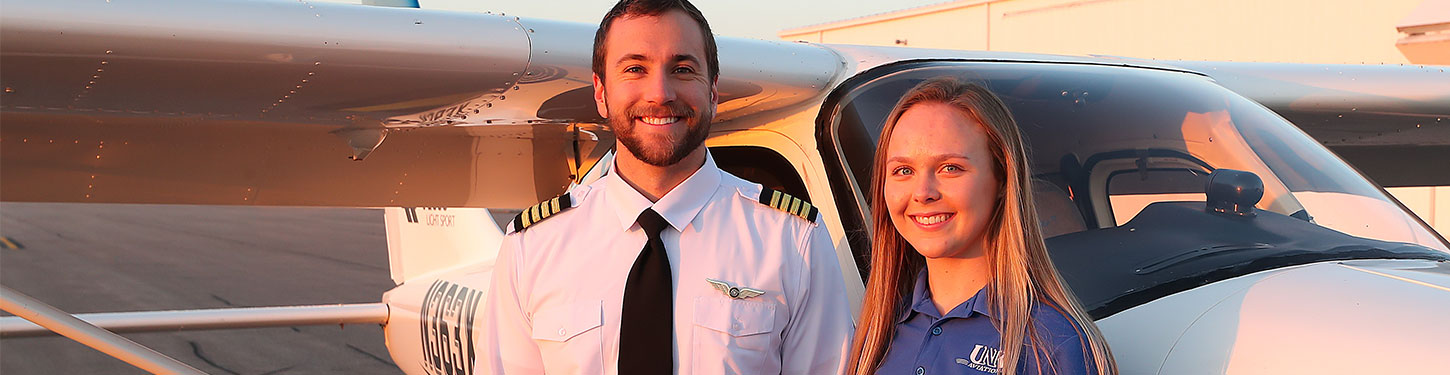 Two people pose for a photo outside of a small aircraft