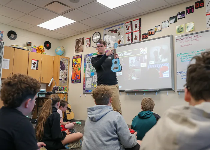 a UNK Music student holds up an instrument in front of a class of children