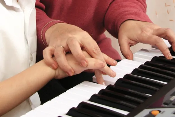 a close up of a teacher and students hands on a piano