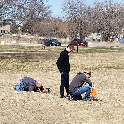 a team readies their rocket for launch while a man lays on the ground setting up a camera