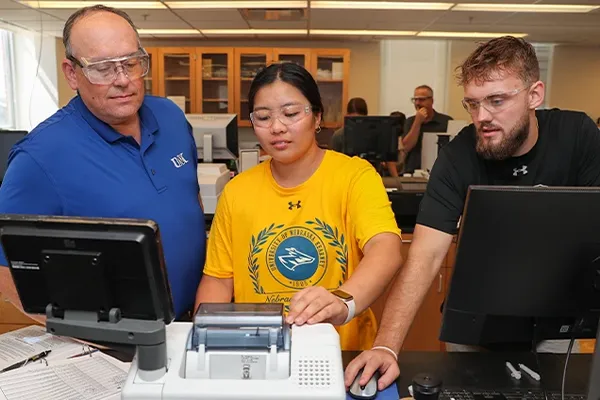 a professor and two students work with lab equipment