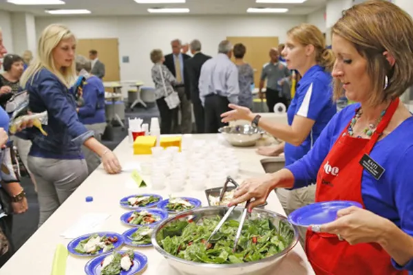 a woman serves salad to a group of students