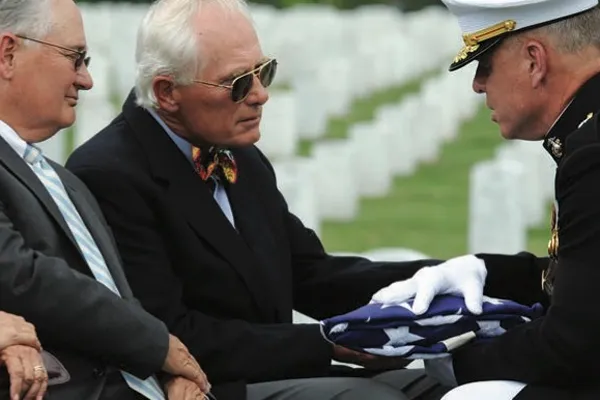 a soldier gives a folded flag to a man at a funeral