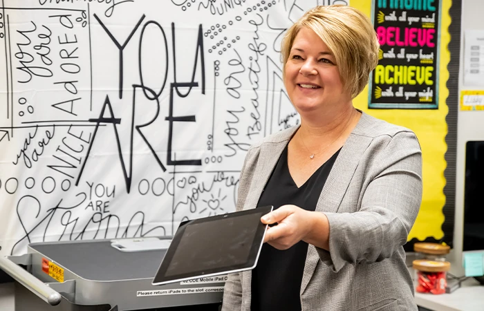 a teacher holds out a tablet in a classroom