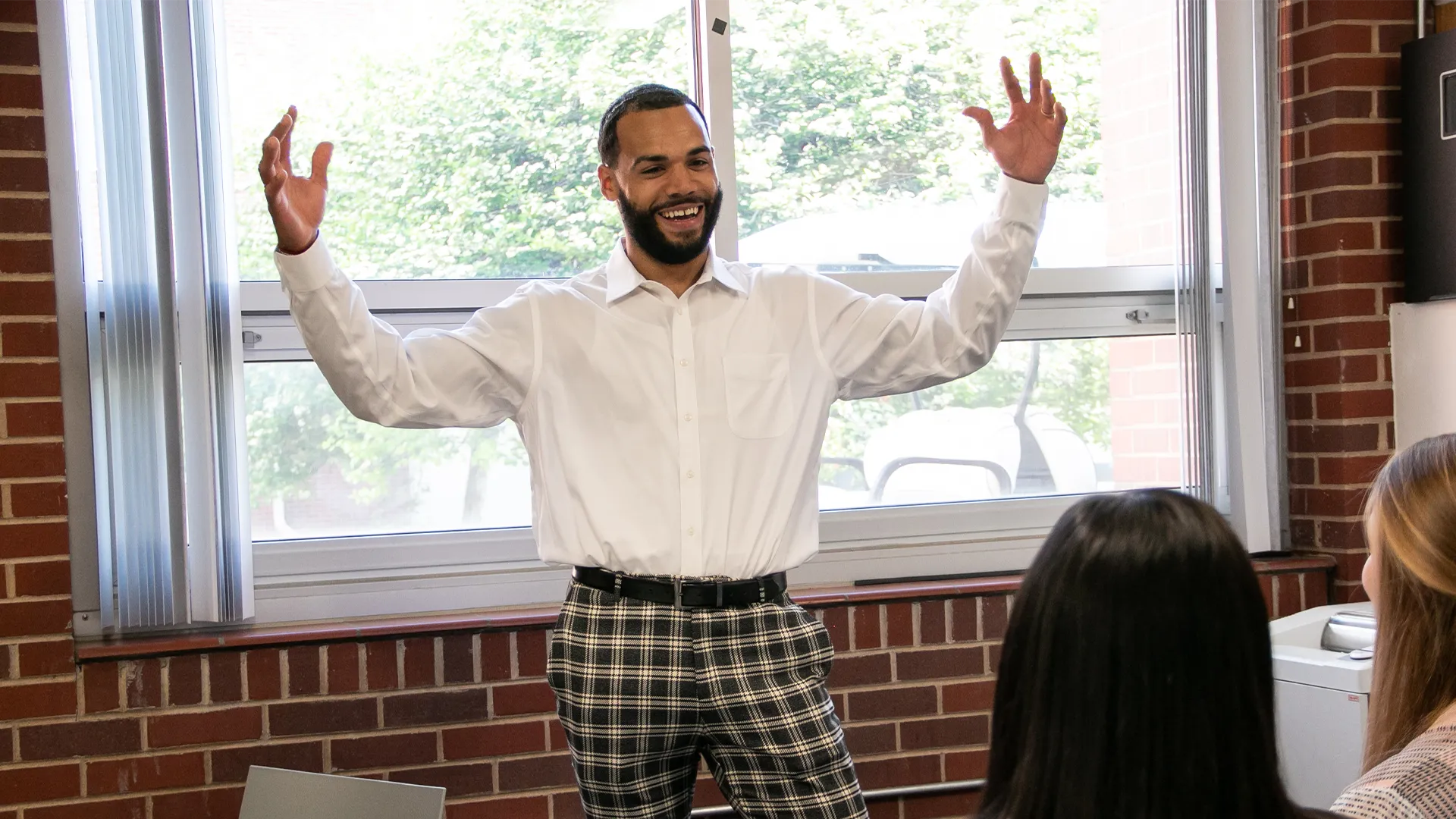 a man raises his arms while speaking to a room of people