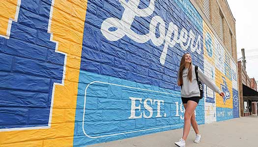 student walking in front of a UNK theme mural