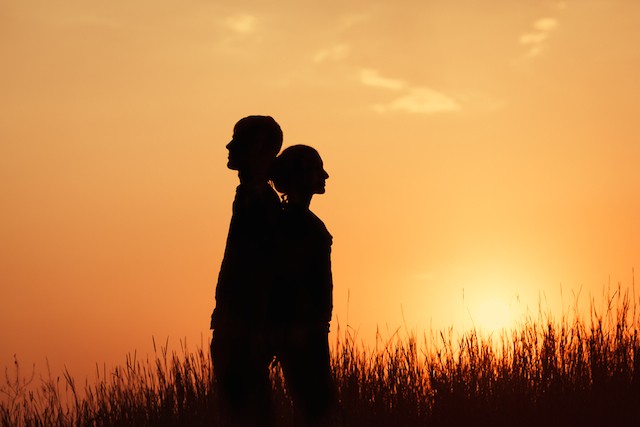 silhouette of man and woman standing in field of grass