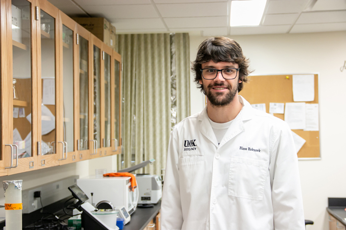 M.S. Biology student, Blase Rokusek, in UNK Biology lab coat standing for photo in UNK Biology lab.