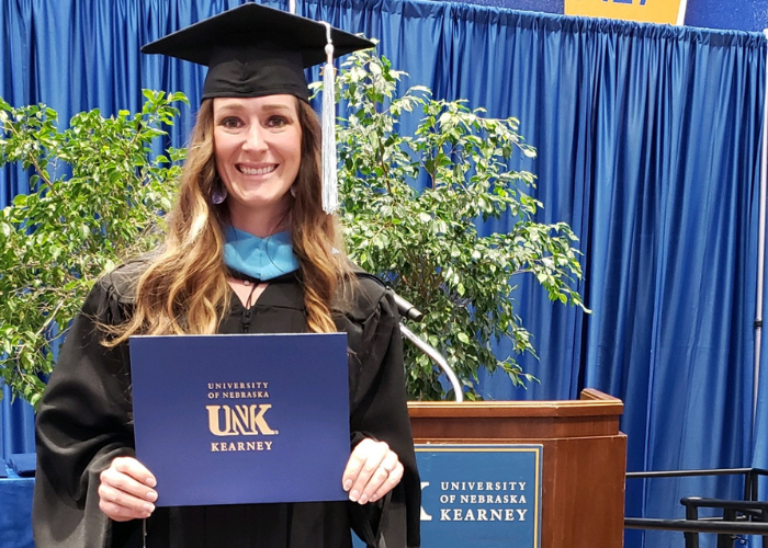 Kelsey Walker holds her diploma on UNK's commencement stage.