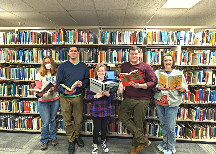 Library staff members holding books in front of bookshelf.