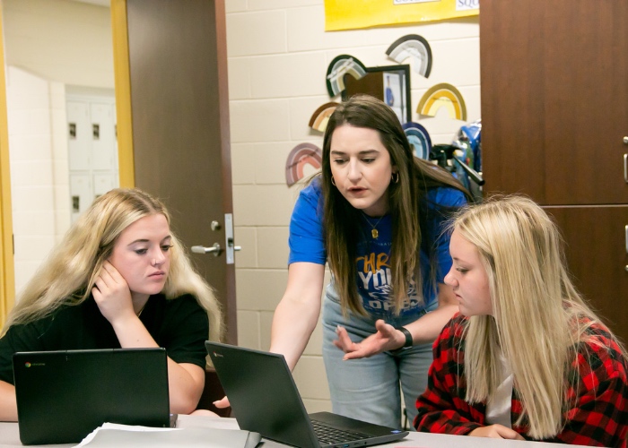 Teacher working with two students at laptops.