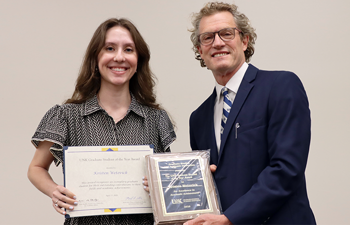 Kristen Wetovick receiving the UNK Graduate Student of the Year Award from Graduate Dean Ellis, both smiling and holding awards.