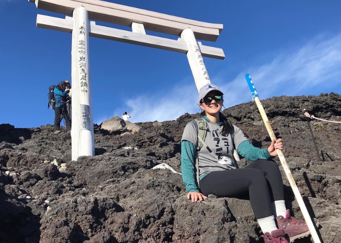 Woman sitting on mountain with walking stick.