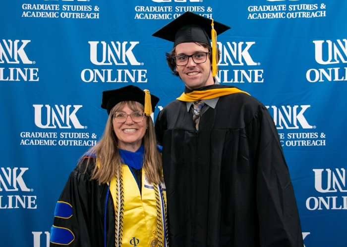 Professor and graduate pose in cap and gown.