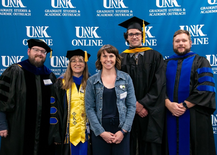 Biology faculty and graduate pose in front of backdrop.