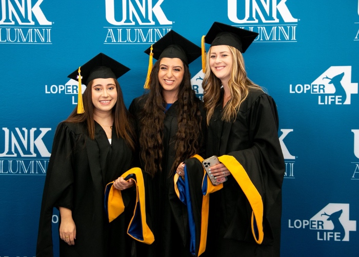 Three graduates posing in front of backdrop.