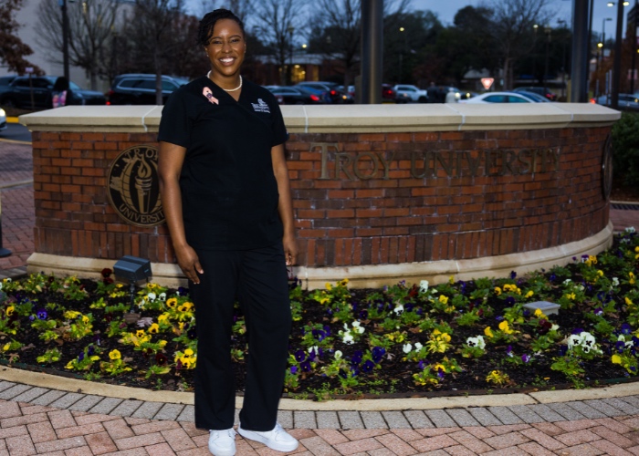 Woman in scrubs standing in front of nursing school sign.