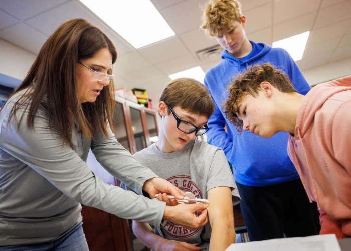 Chelle working with three students in science classroom.