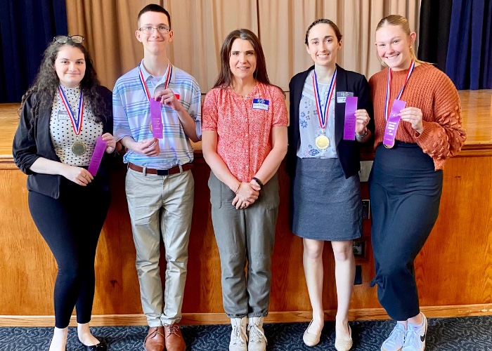 Chelle with four students holding purple ribbons at a science fair.