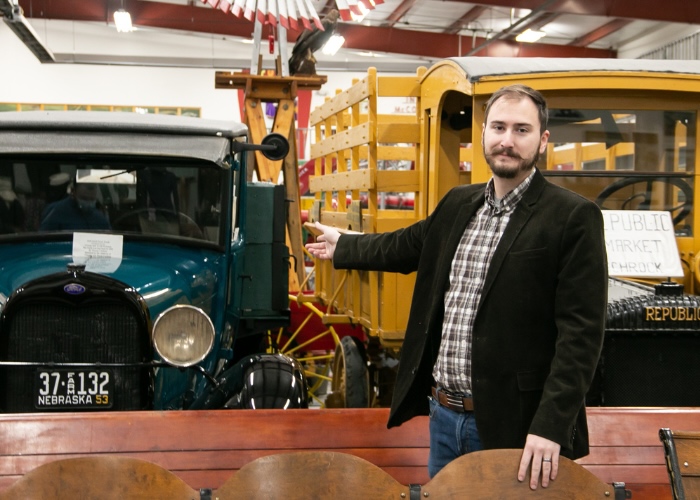 Man gesturing at vintage vehicles in a museum.