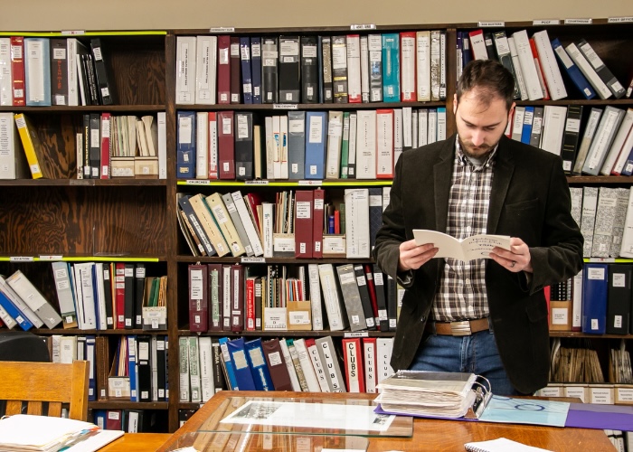 Man reading booklet in front of bookshelves. 