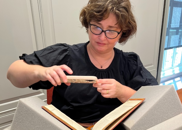 Christy taking photo of book with phone at Harvard's library.