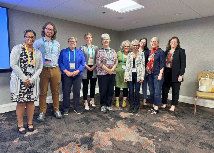 Group photo of nine women and one man with lanyard name tags on smiling at the camera.