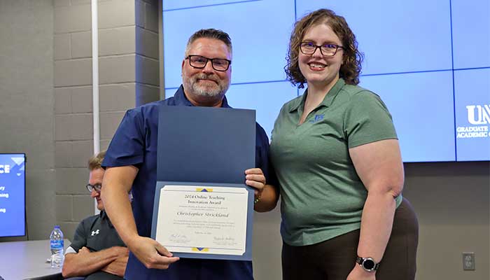 Dr. Christopher Strickland receiving the certificate for Outstanding Innovation in Online Teaching award from the previous year's winner, Dr. Amanda Sladek.
