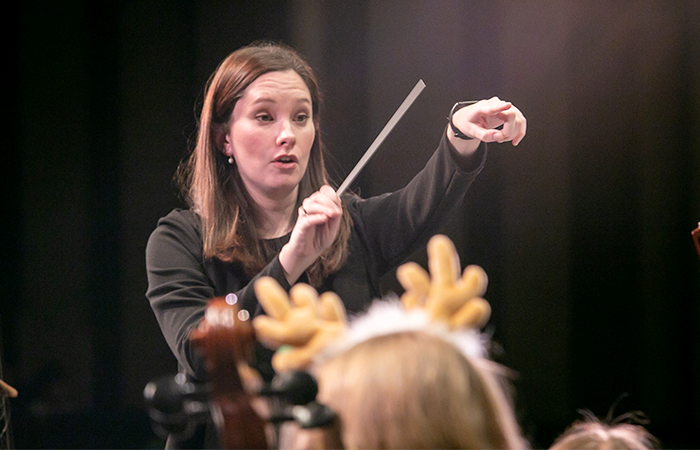 A woman conductor leads an orchestra concert. 