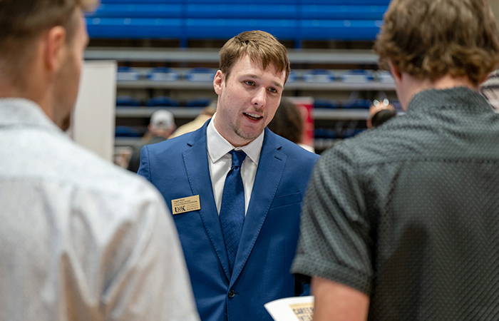 Man in suit and tie talking with two other men.