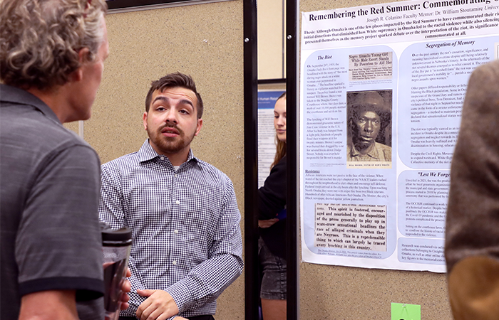 Joseph Colanino, UNK graduate student presenting research during UNK's poster session of Research Day, discussing the historical context of the Red Summer with attendees.
