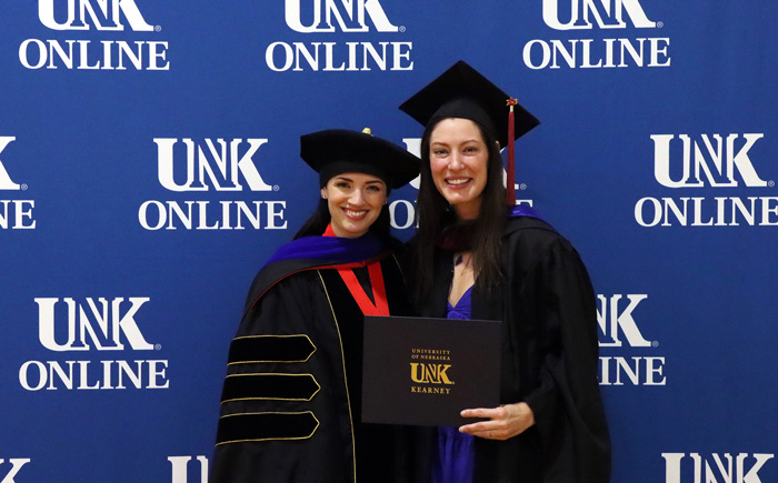 Kattie Sadd with her advisor Dr. Tiffani Luethke at UNK's Online graduation ceremony, smiling for the camera with a diploma in her hand