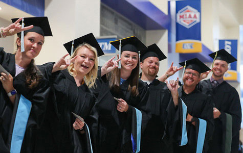 A group of graduate students wearing caps and gowns smiling at UNK's commencement ceremony.