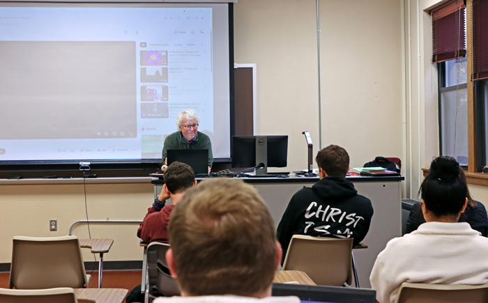 Rick Brown leans on the table at the front of his college writing class.